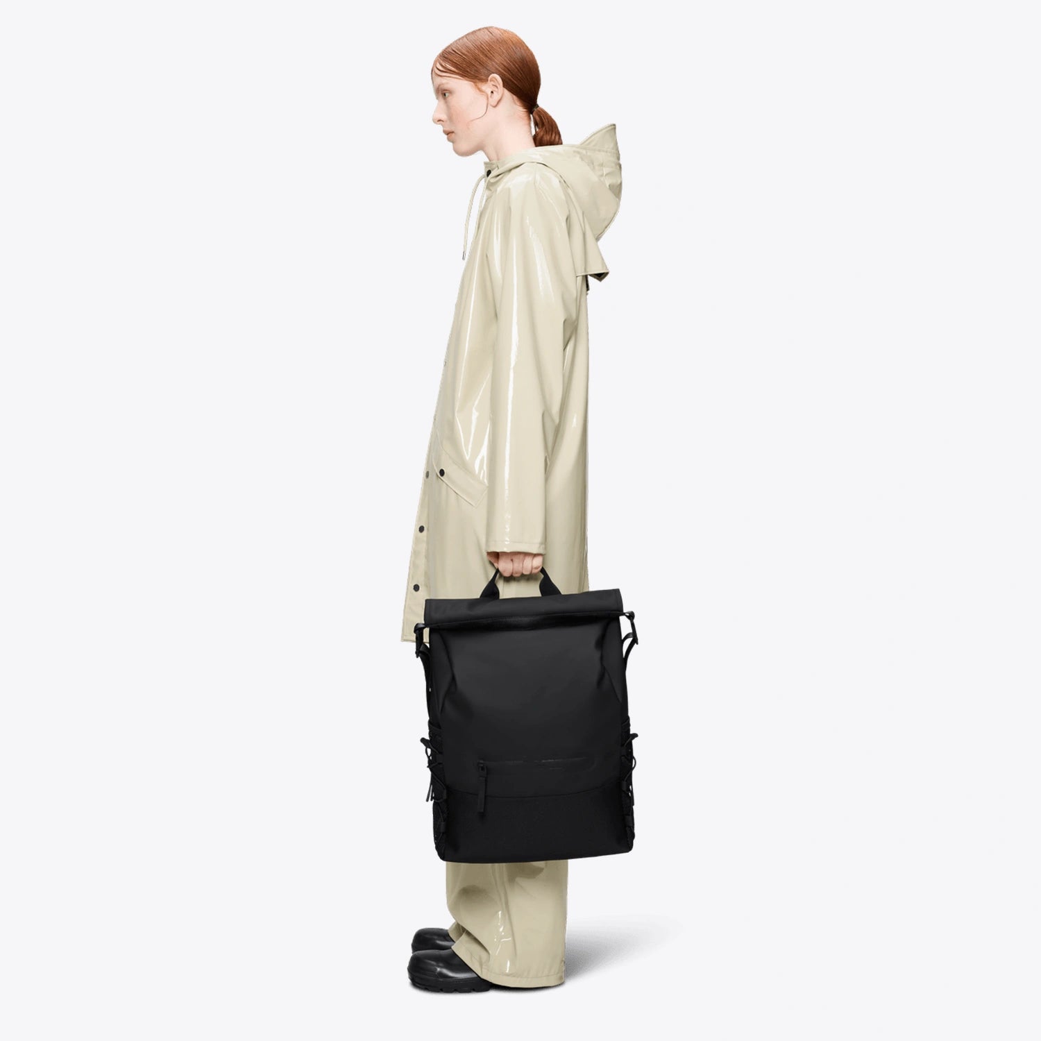 Trail Mountaineer Rolltop Black Backpack showcased with a model wearing a raincoat.