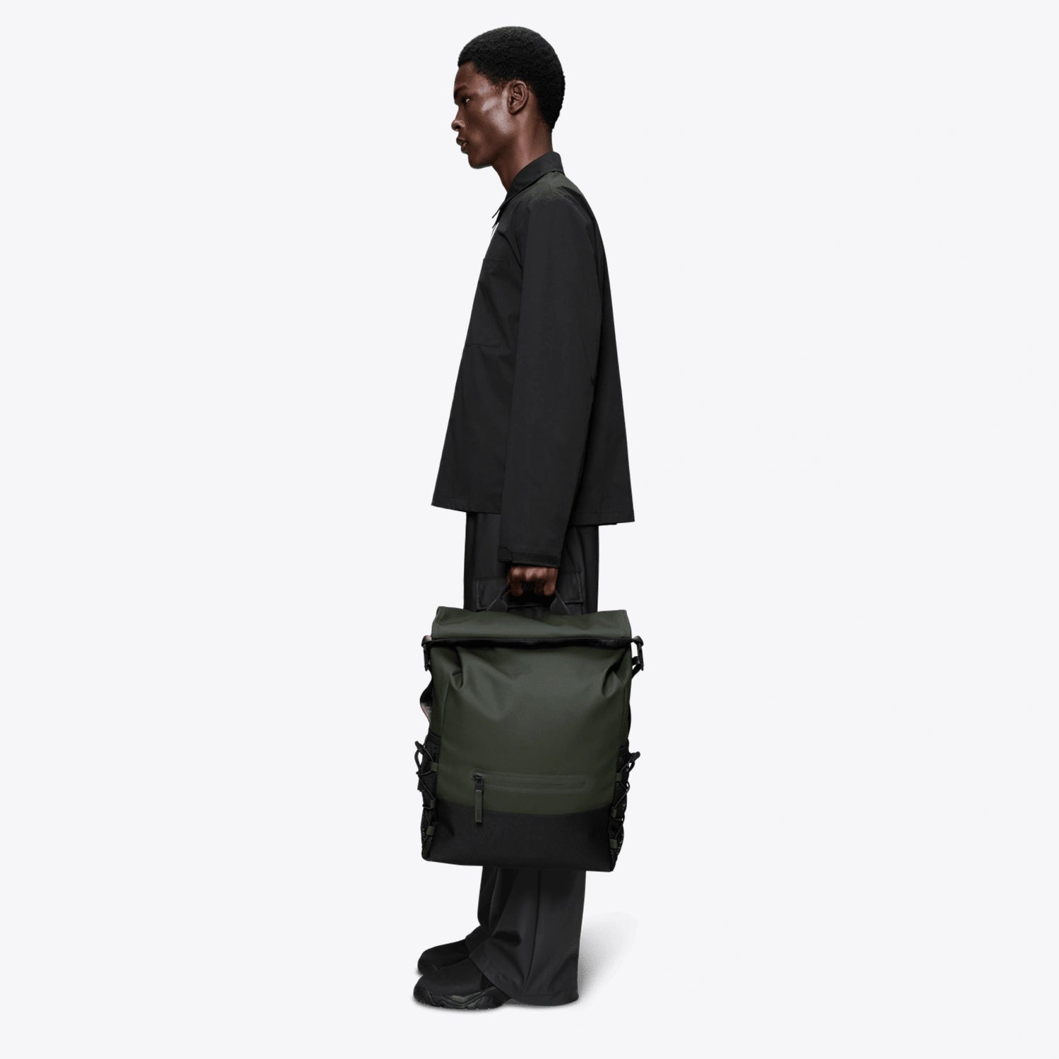 Side view of a model holding the Trail Mountaineer Rolltop Green Backpack, showcasing its stylish and practical design.