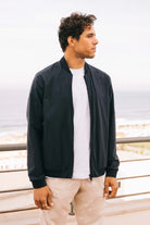 Campo II Navy Jacket model showcasing lightweight, windproof, and water-resistant features by the ocean.