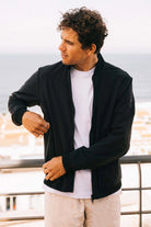 Man wearing Campo II Graphite Jacket, a lightweight summer jacket, outdoors with a coastal view.
