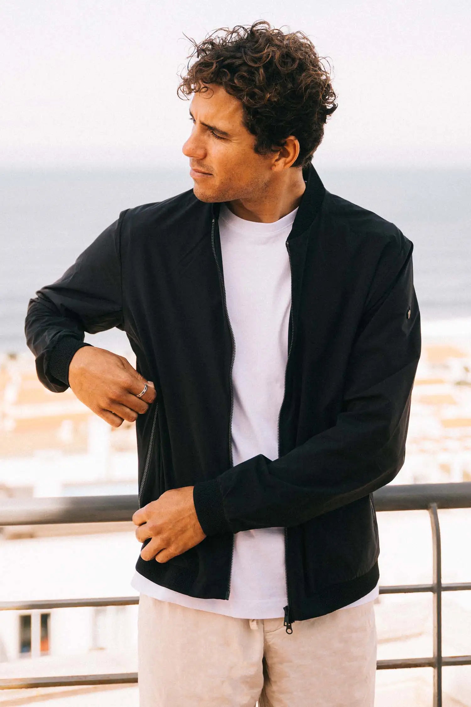 Man wearing Campo II Graphite Jacket, a lightweight summer jacket, outdoors with a coastal view.