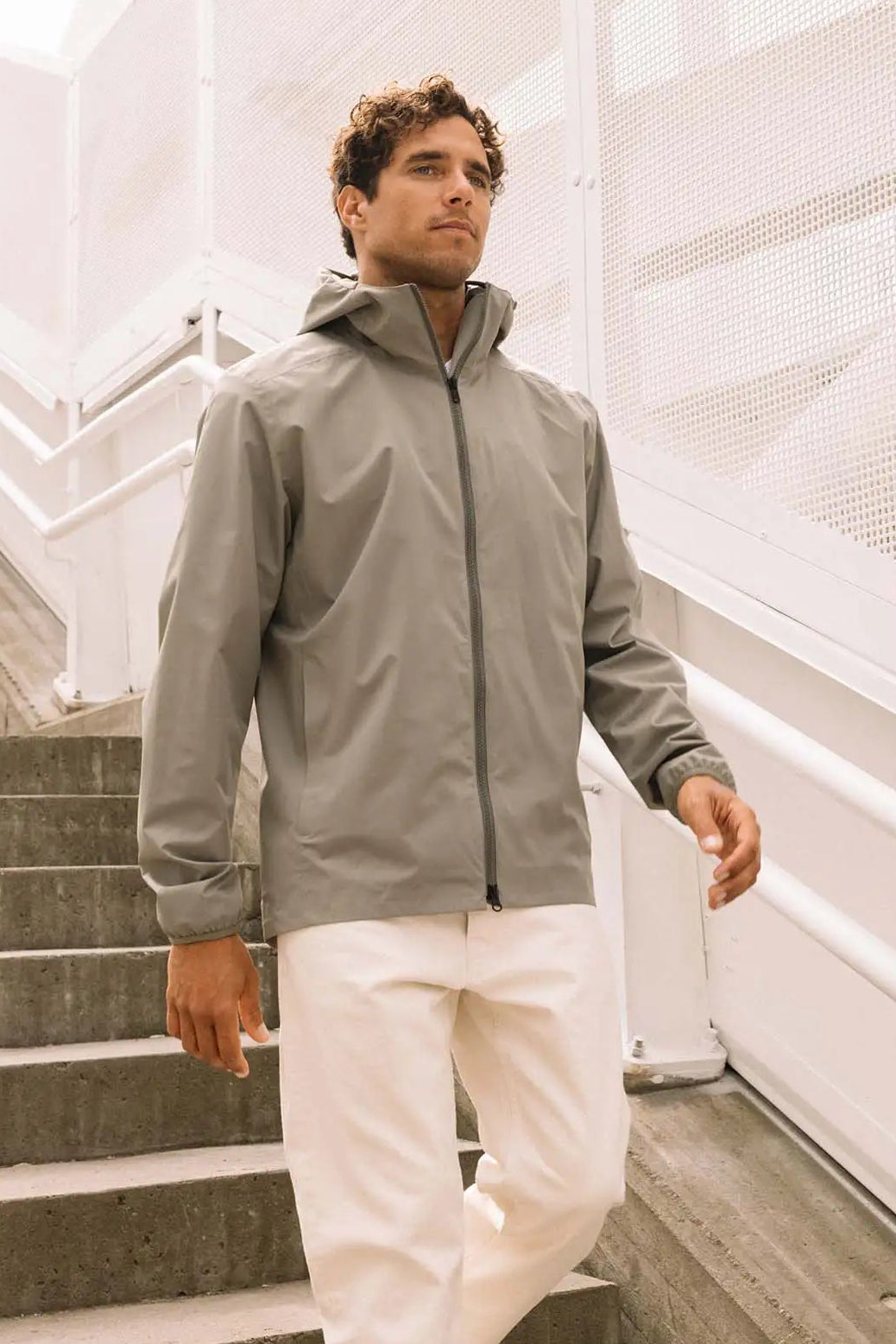 Model wearing the Hood II Light Green Jacket on stairs. Lightweight, windproof, and waterproof jacket ideal for spring and autumn.