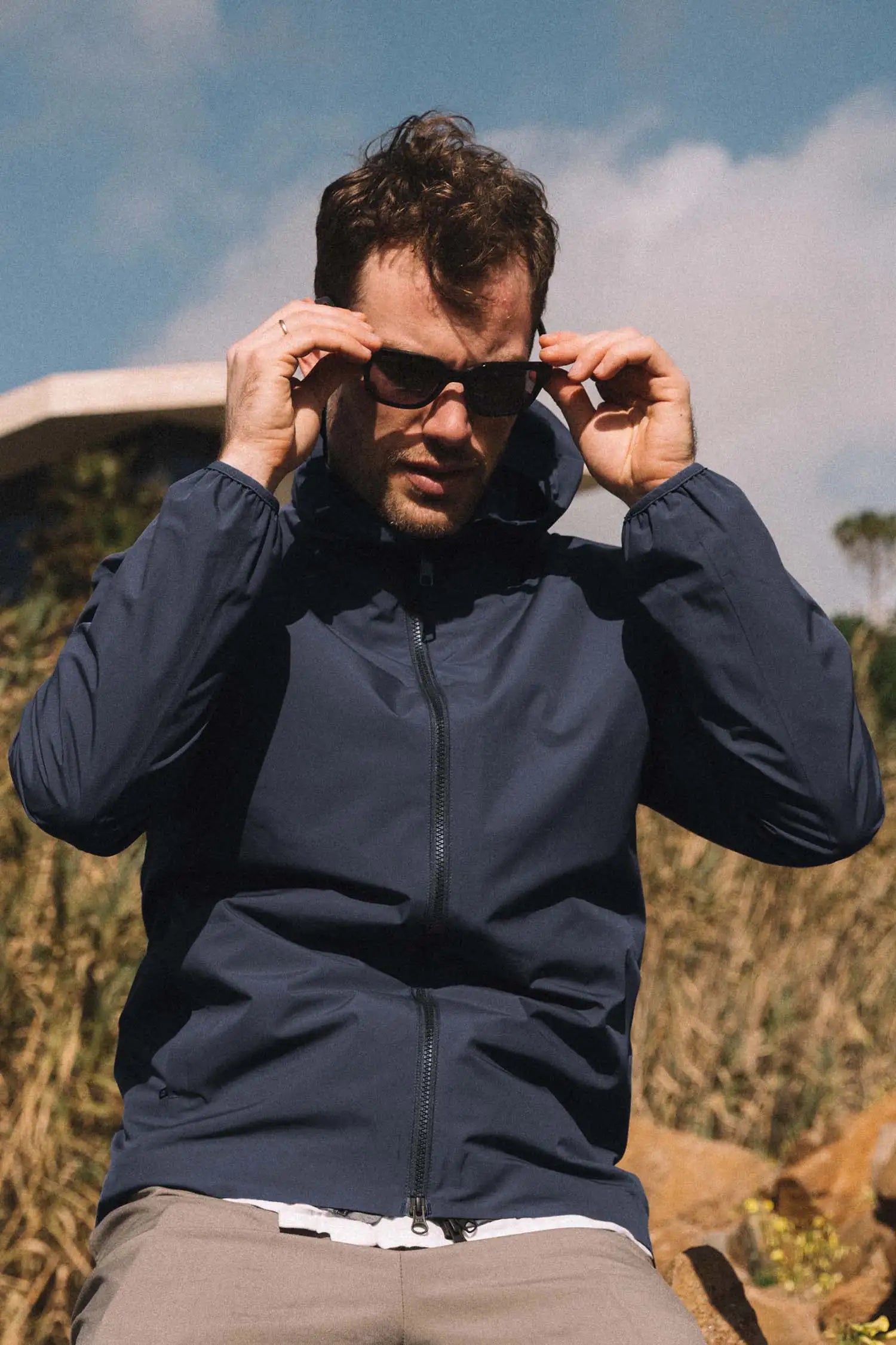 Man wearing Hood II Midnight Jacket and sunglasses outdoors with nature backdrop.
