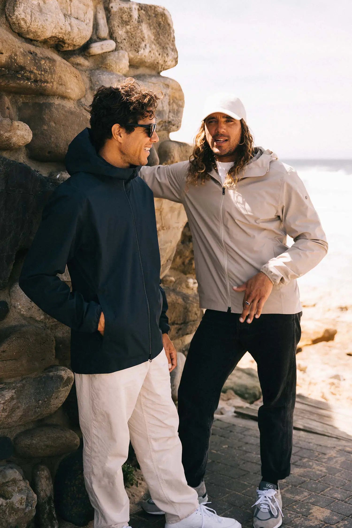 Two men wearing Hood II Midnight Jacket in a casual outdoor setting by the ocean, showcasing style and comfort.