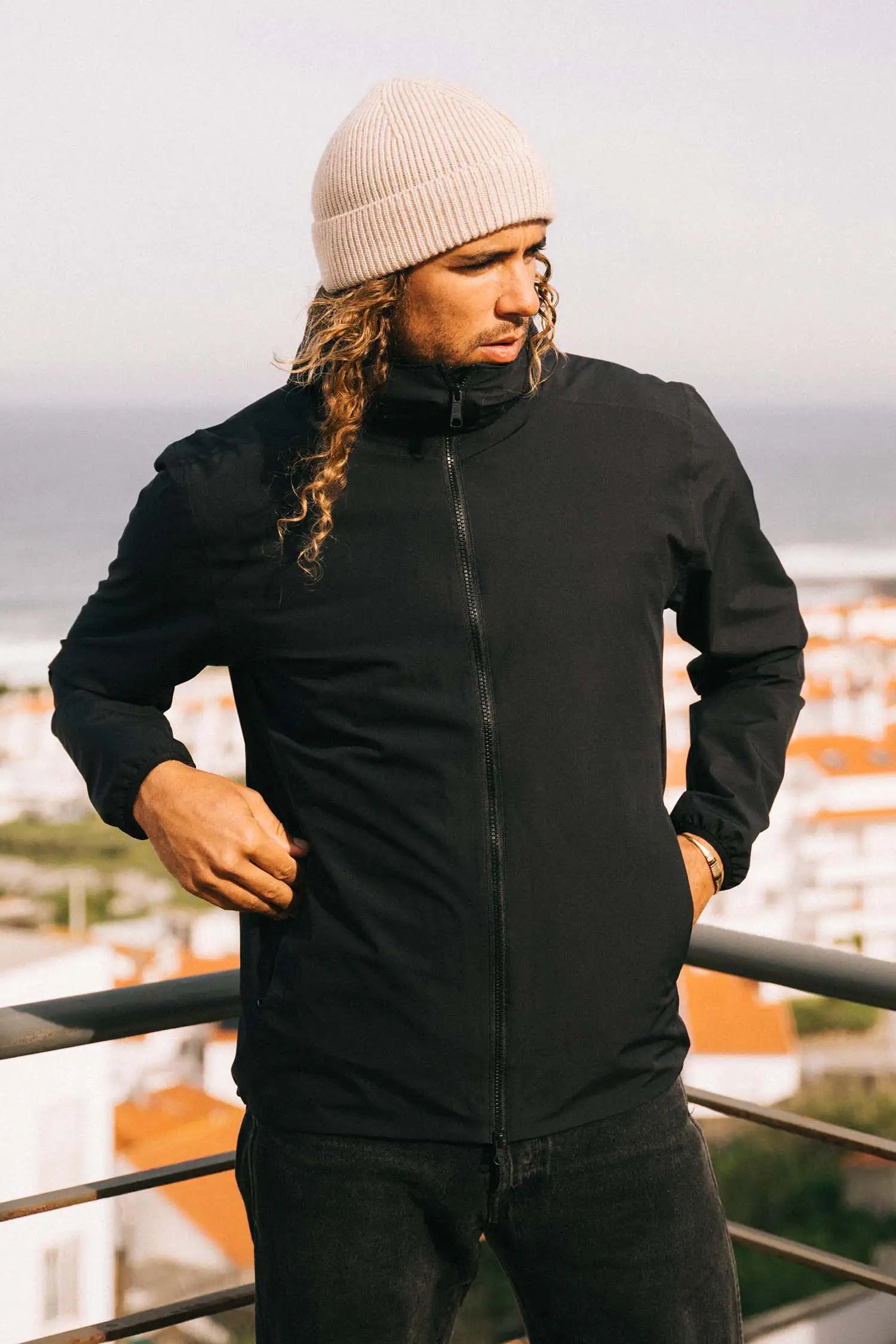 Man wearing a Hood II Onyx Jacket, showcasing its lightweight, windproof design against a coastal backdrop.