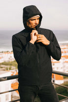 Man wearing Hood II Onyx Jacket, standing on balcony with scenic background.