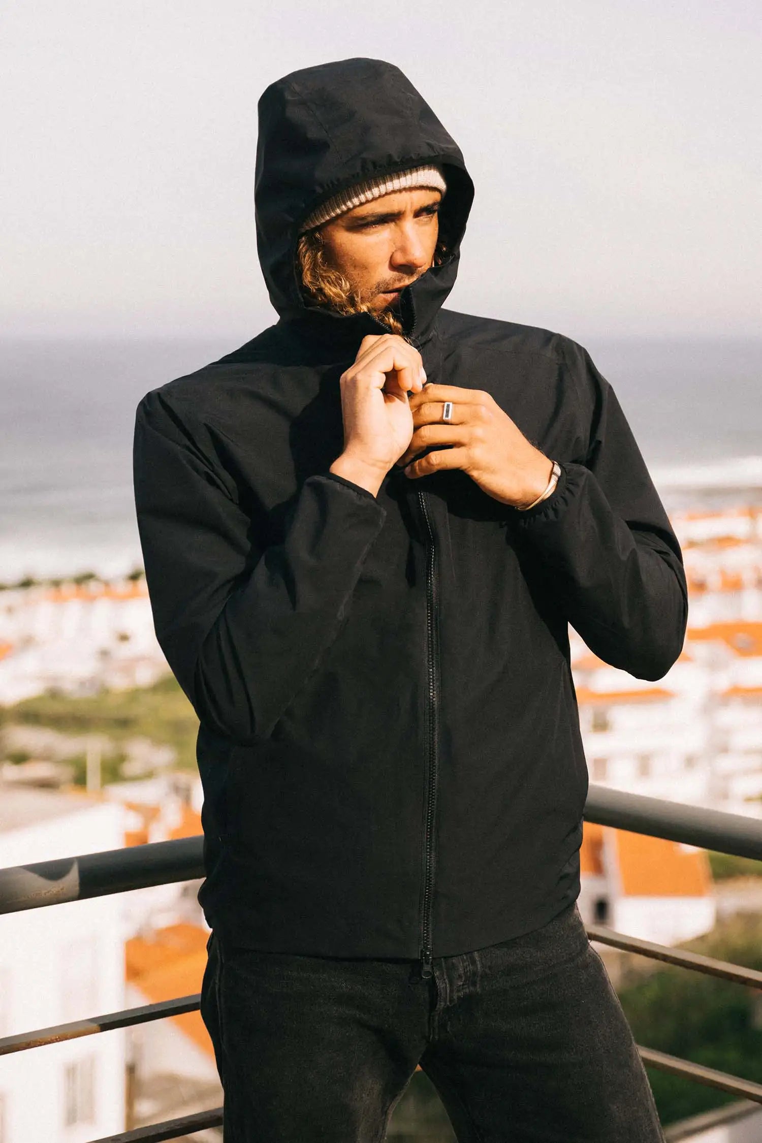 Man wearing Hood II Onyx Jacket, standing on balcony with scenic background.