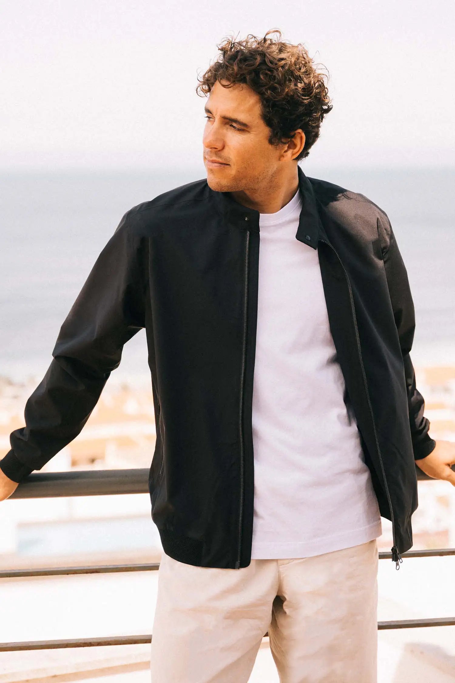Man wearing a Plain II Onyx Jacket in a scenic outdoor setting near the sea.