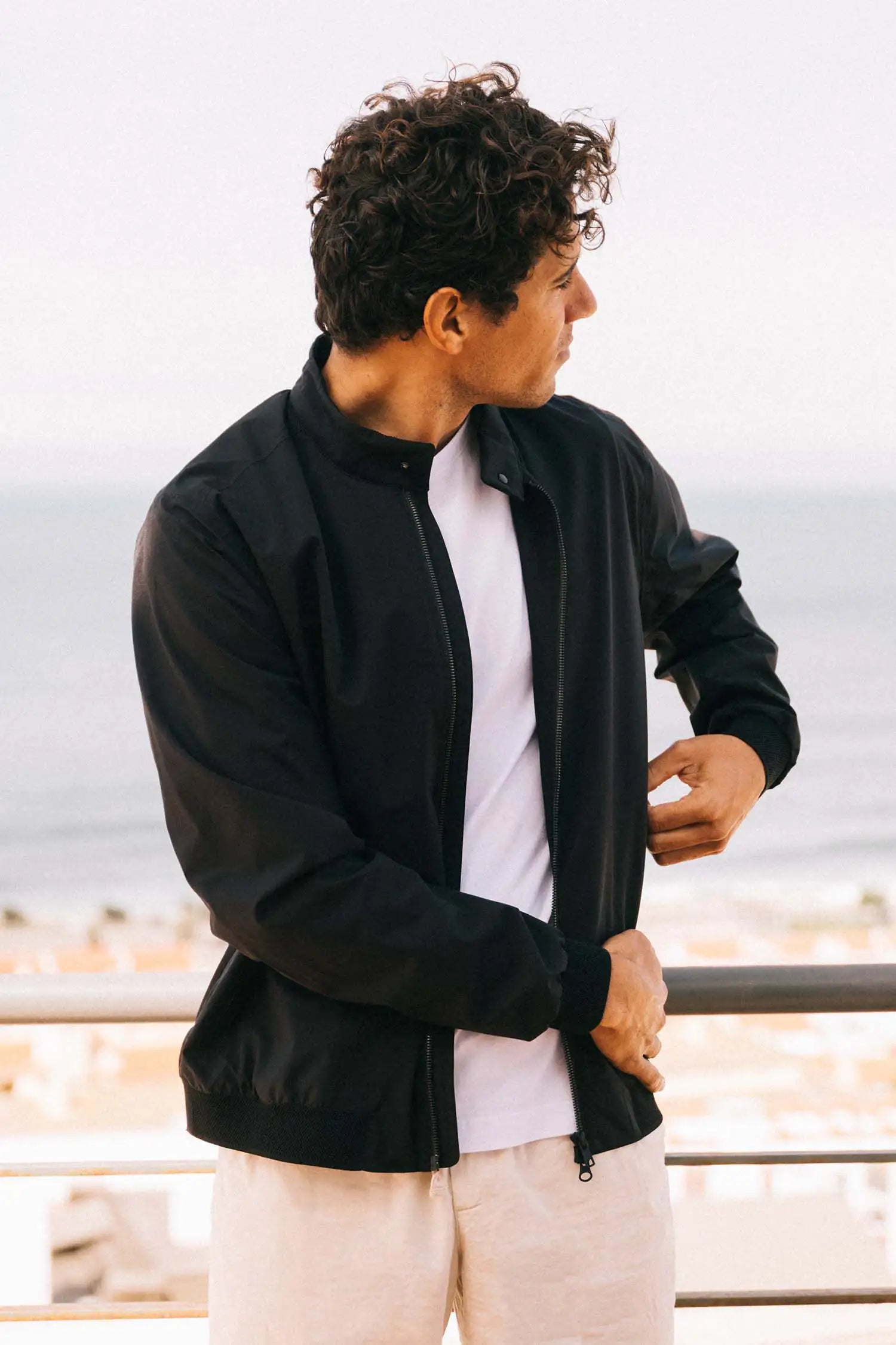 Model wearing the Plain II Onyx Jacket by the sea in a modern city look.