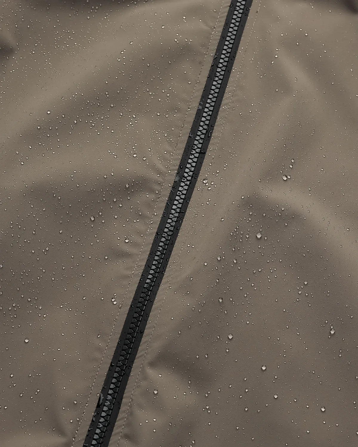 Close-up of the Era Apex Sand Jacket showing water droplets on the fabric, highlighting its waterproof features.