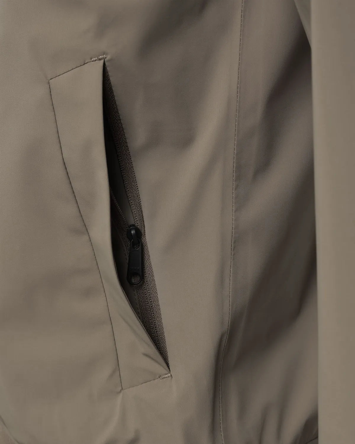 Close-up of a zippered pocket on the Era Apex Sand Jacket, showcasing windproof and waterproof fabric features.