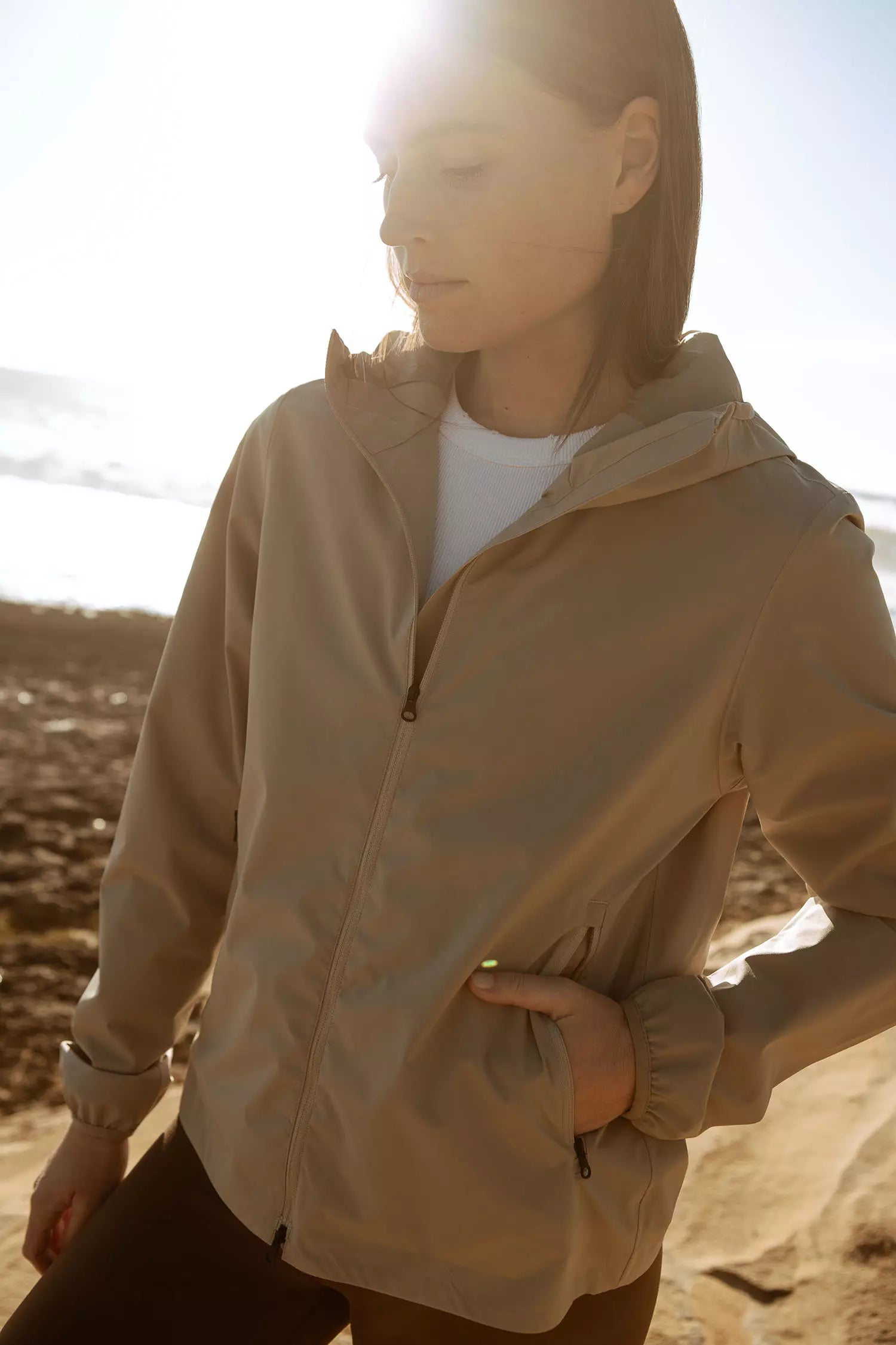 Model wearing the Veil II Khaki Jacket on the beach with sunlight in the background.