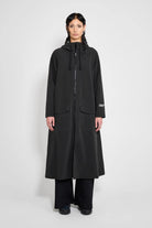 Mosebacke Long Patch Black Raincoat displayed on a model, featuring a stylish A-line silhouette and adjustable hood.