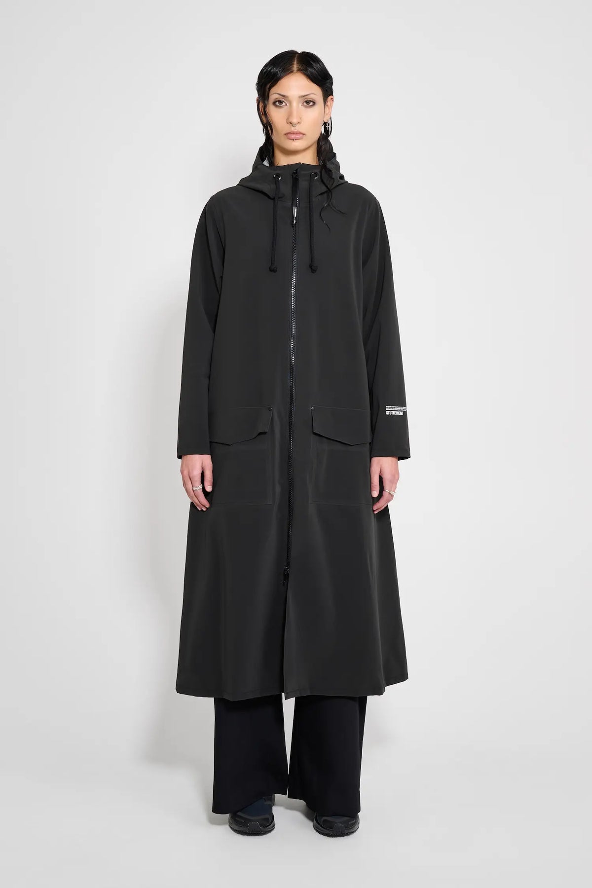 Mosebacke Long Patch Black Raincoat displayed on a model, featuring a stylish A-line silhouette and adjustable hood.