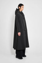 Mosebacke Long Patch Black Raincoat displayed on a model, showcasing its A-line silhouette and adjustable hood.