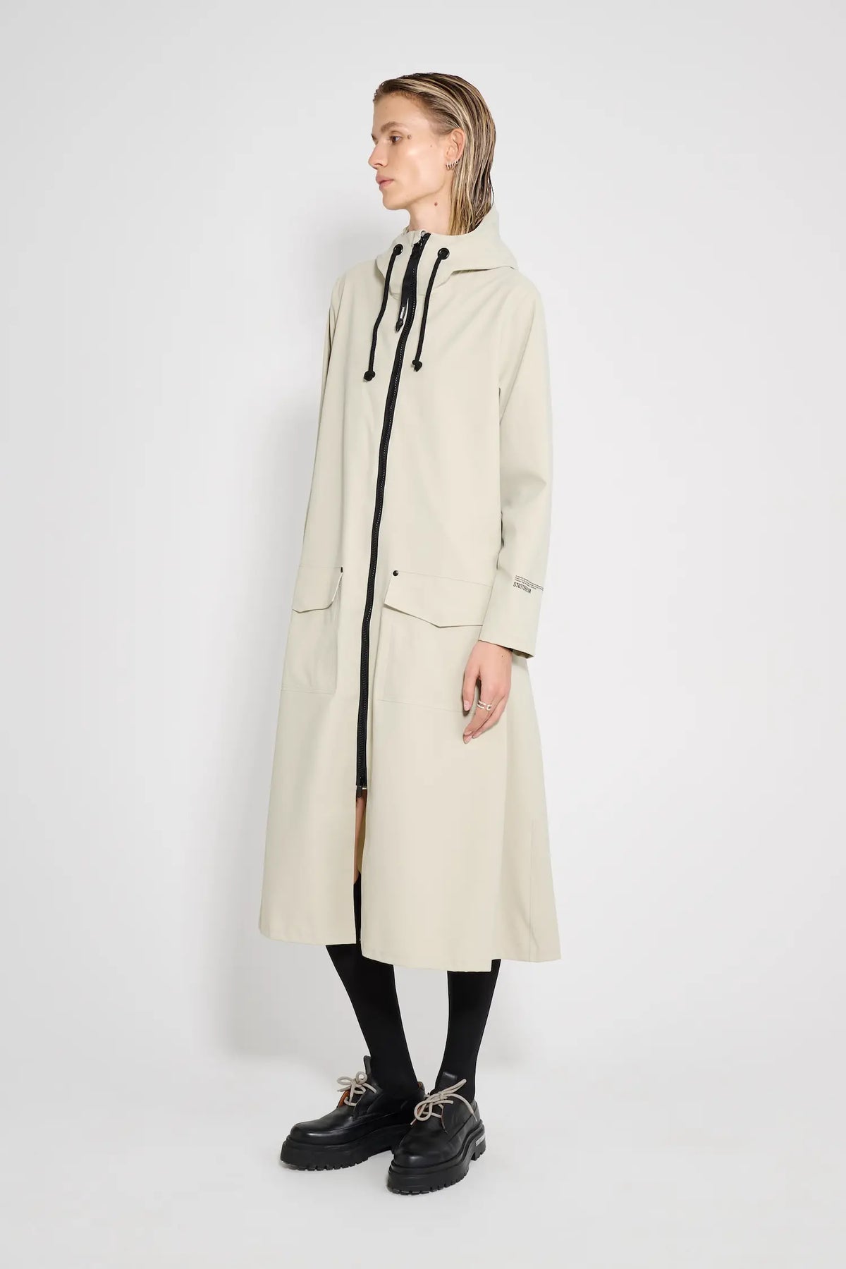 Mosebacke Long Patch Pelican Raincoat displayed on a model, showcasing its A-line silhouette and waterproof design.