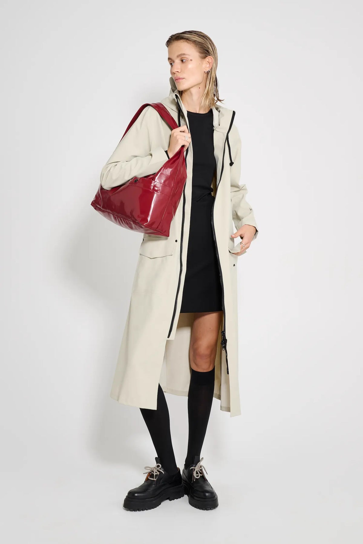 Model wearing Mosebacke Long Patch Pelican Raincoat with a red bag, showcasing a stylish rain protection.
