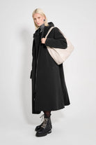Mosebacke Long Matte Black Winter Coat worn by model with a beige bag and stylish boots on a white background.