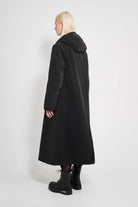 Mosebacke Long Matte Black Winter Coat worn from the back, showcasing its A-line silhouette and adjustable hood.