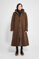 Mosebacke Long Matte Dark Brown Winter Coat modeled by a woman, showcasing adjustable hood and two-way zipper.