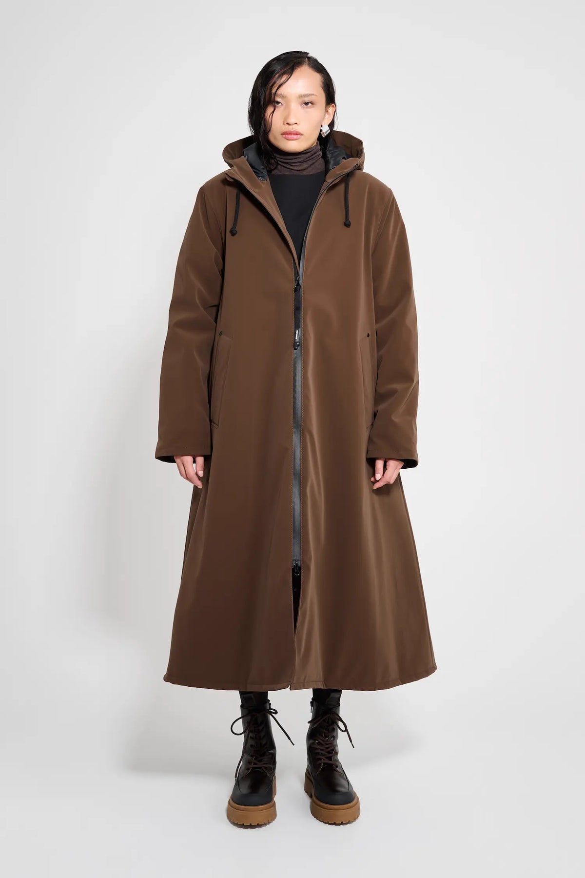 Mosebacke Long Matte Dark Brown Winter Coat modeled by a woman, showcasing adjustable hood and two-way zipper.