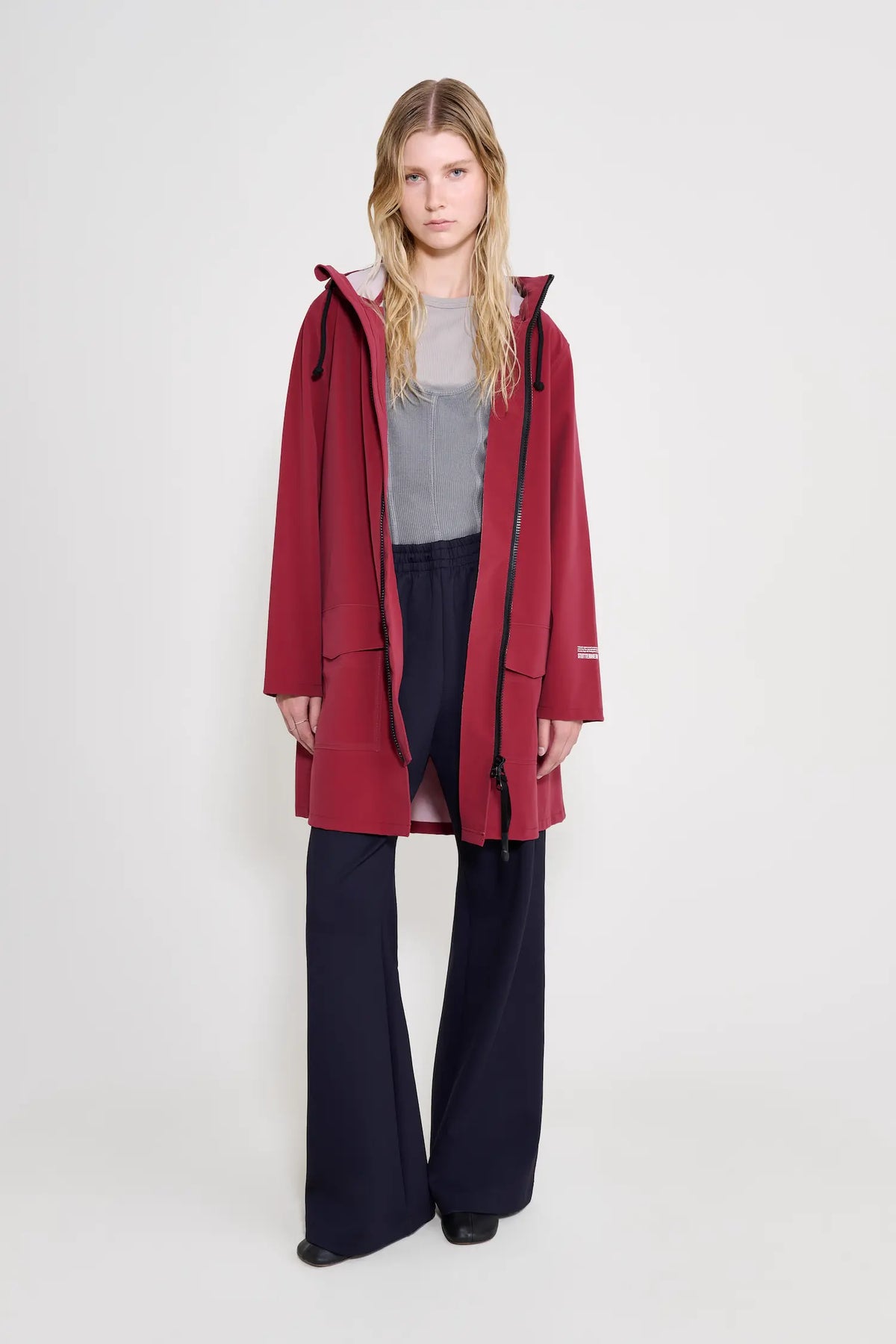 Mosebacke Patch Burgundy Raincoat worn by a model with a drawstring hood and flared pants.