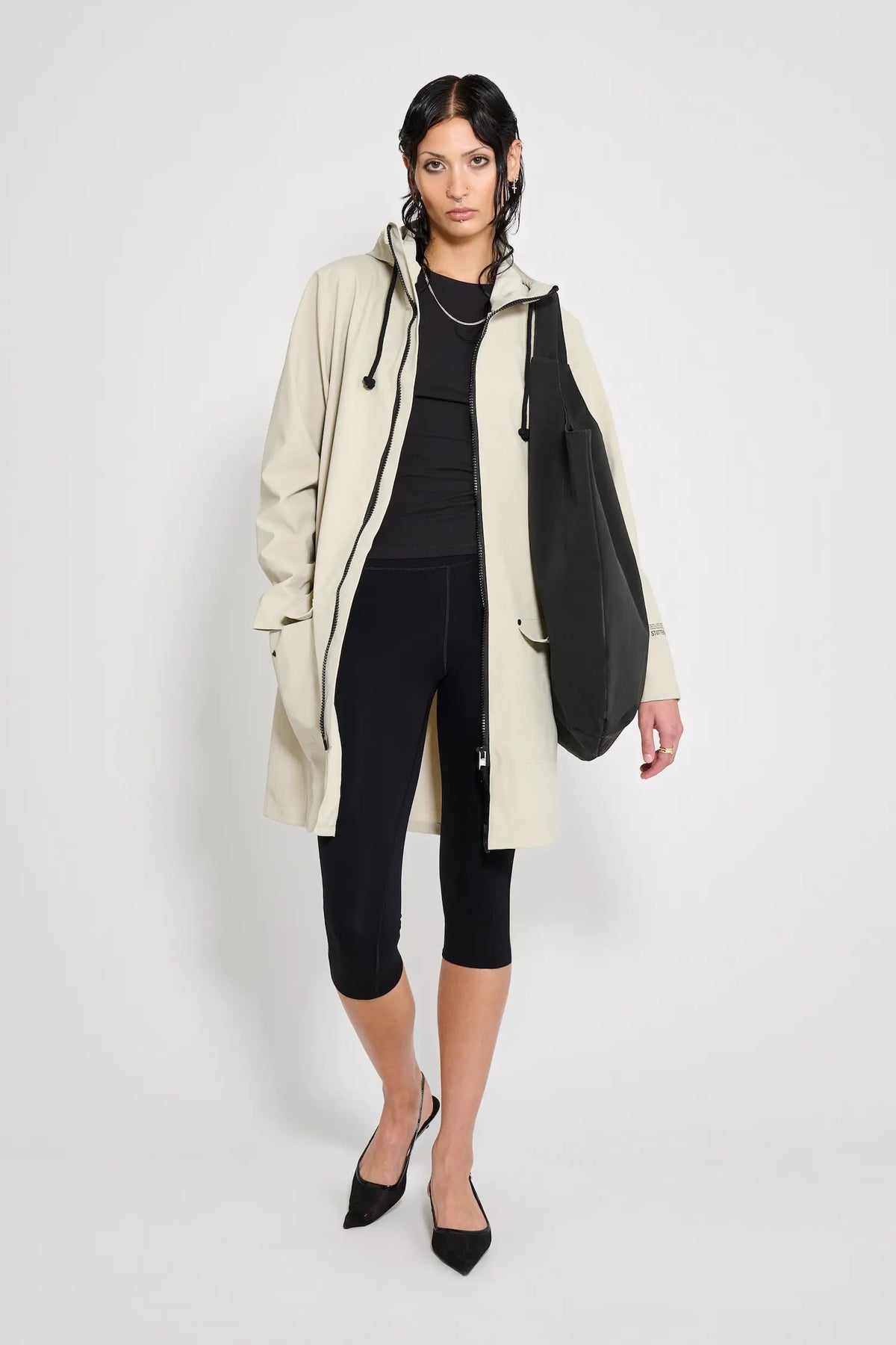 Model wearing Mosebacke Patch Pelican Raincoat with adjustable hood and black bag.