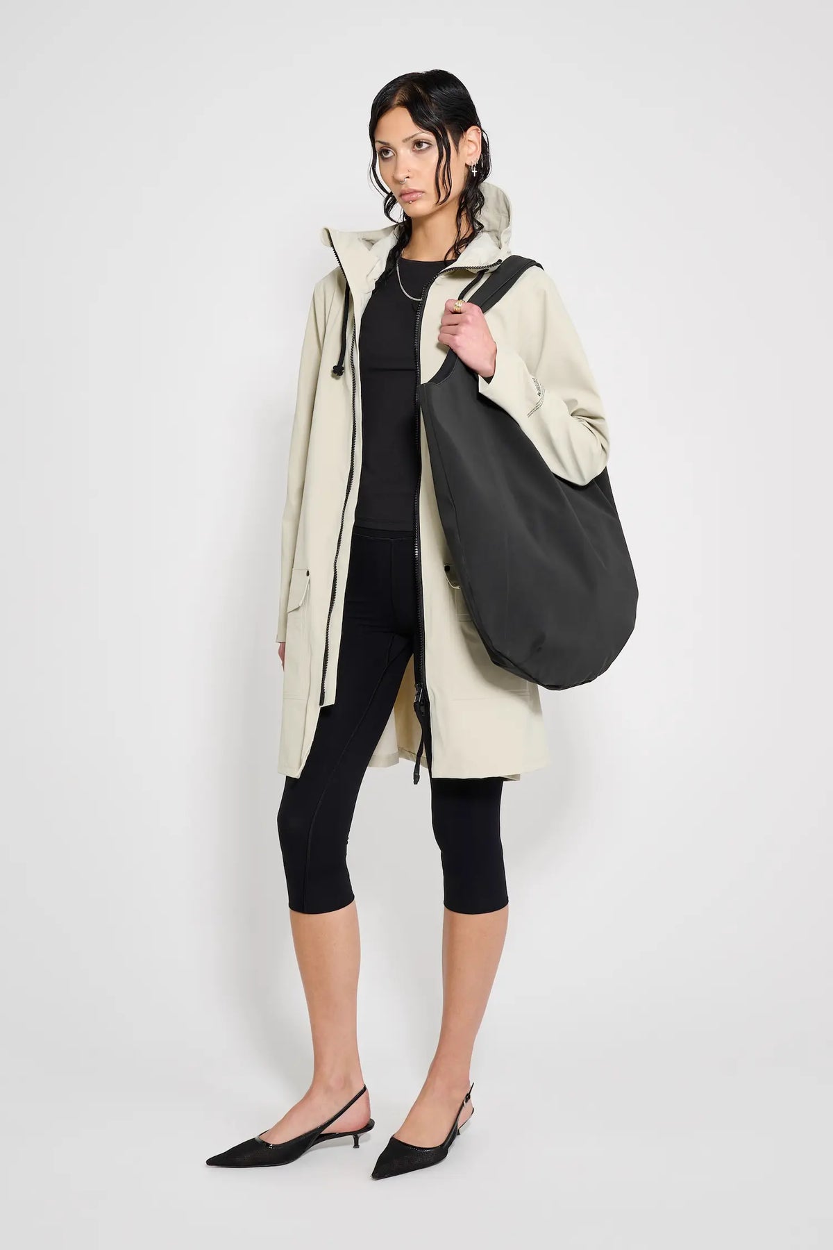 Model wearing Mosebacke Patch Pelican Raincoat in beige with a black bag, showcasing its stylish and functional design.