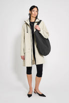 Model wearing Mosebacke Patch Pelican Raincoat in beige with a black bag, showcasing its stylish design and functionality.