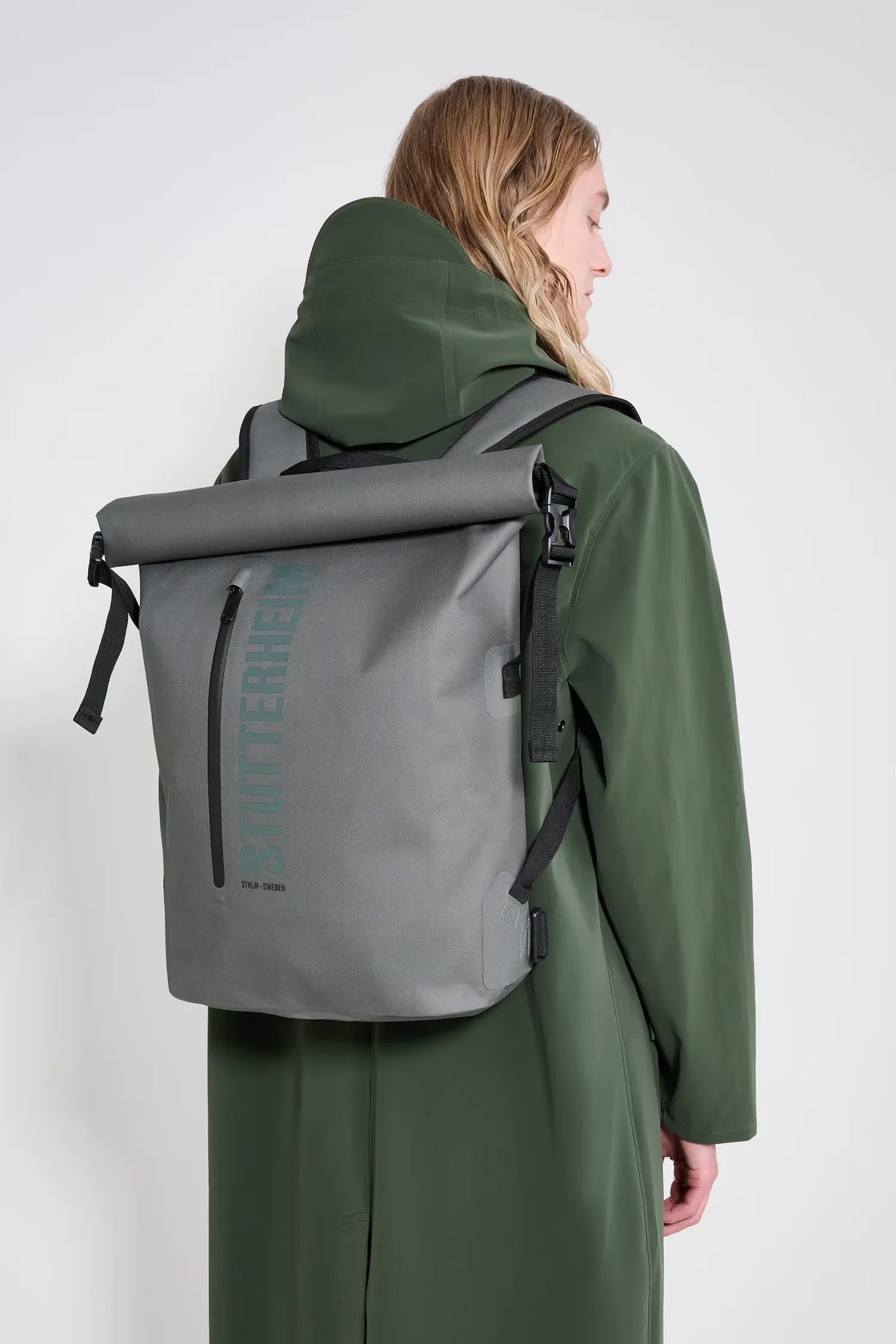 Rain Rolltop 25L Green Backpack worn by a model with a gray coat, showcasing its waterproof design and rolltop feature.