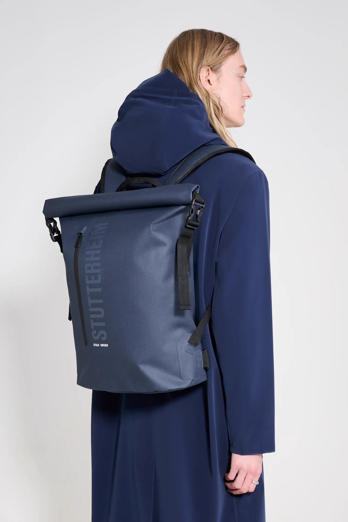 Person wearing Rain Rolltop 25L Navy Backpack, showcasing its waterproof design and rolltop feature.