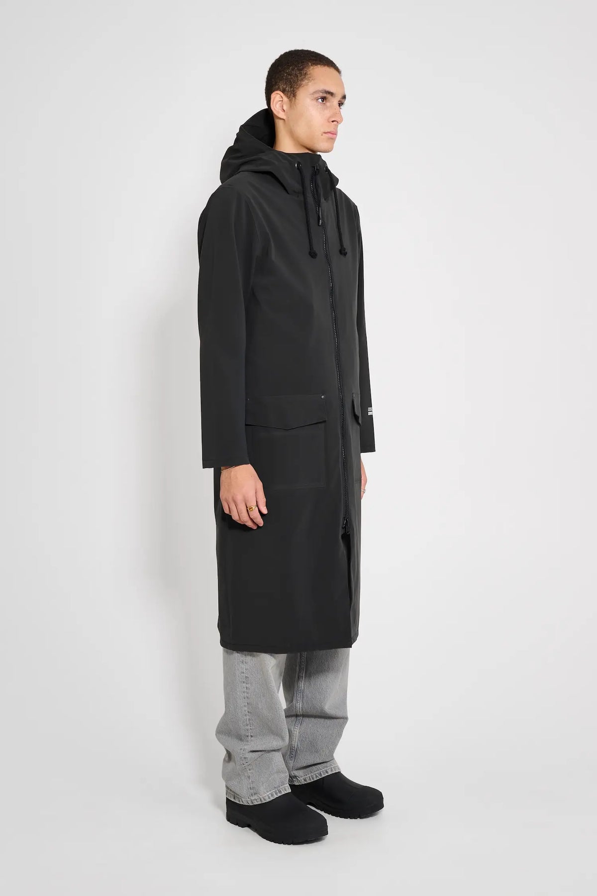 Stockholm Long Patch Black Raincoat displayed on a model, showcasing its oversized fit and adjustable hood.
