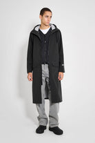 Model wearing the Stockholm Long Patch Black Raincoat, showcasing its straight oversized fit and adjustable hood.