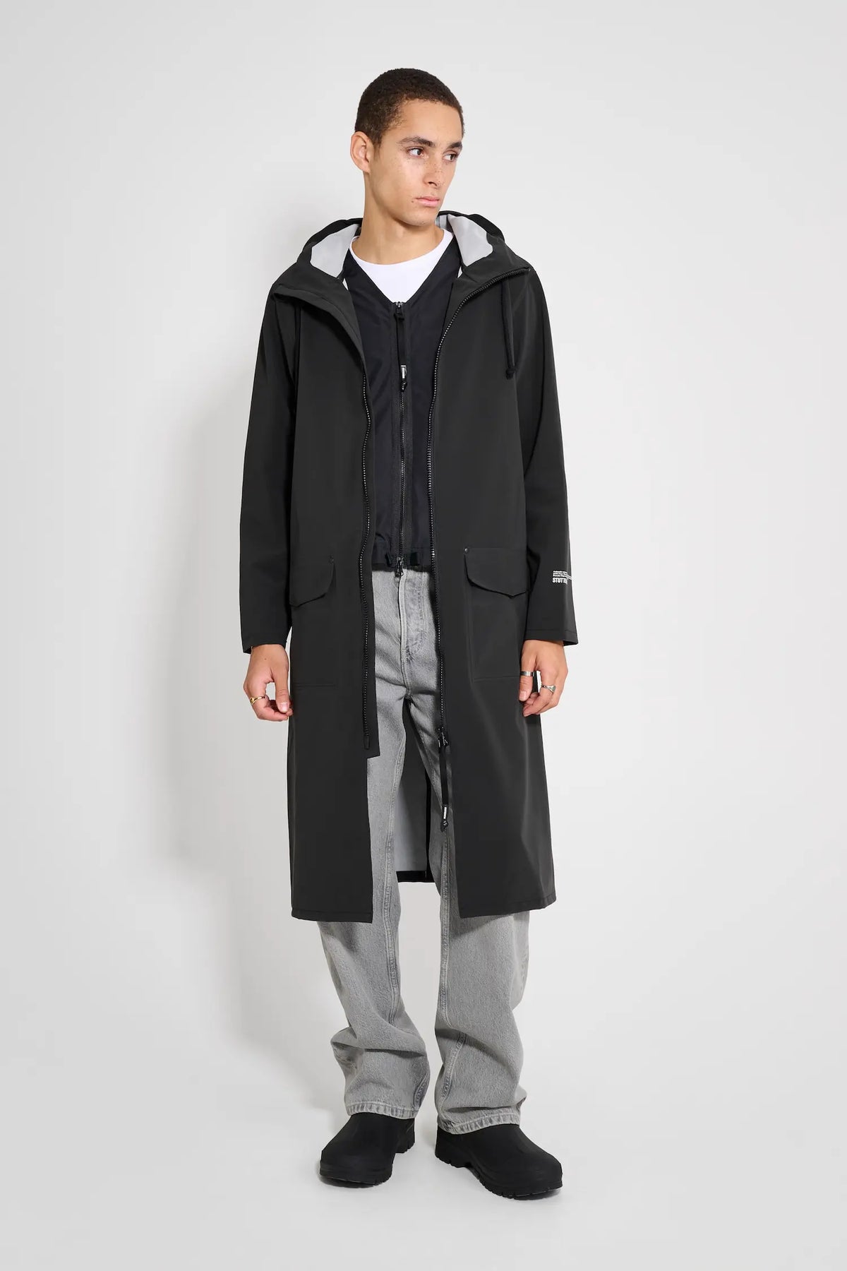 Model wearing the Stockholm Long Patch Black Raincoat, showcasing its straight oversized fit and adjustable hood.