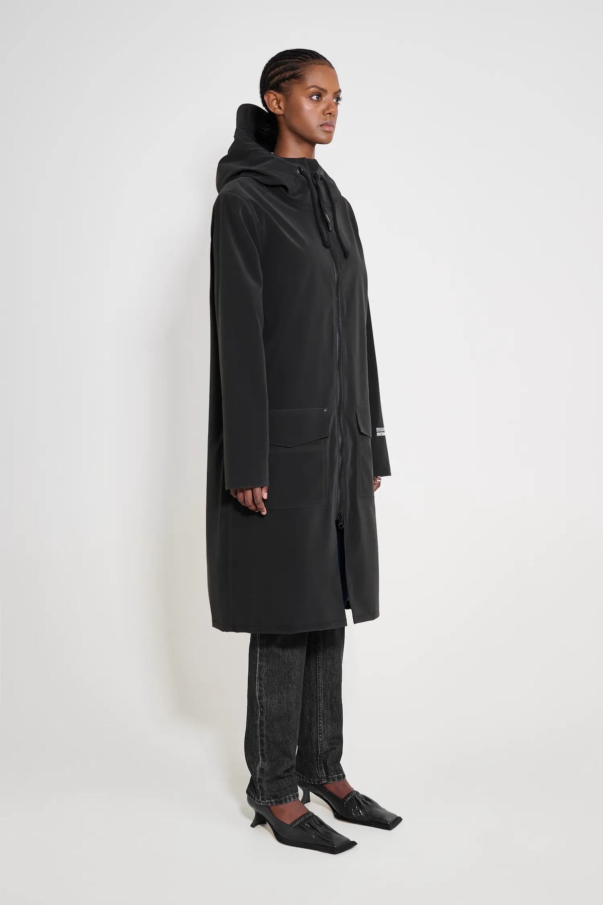 Stockholm Long Patch Black Raincoat worn by a model, showcasing its oversized fit and adjustable hood.