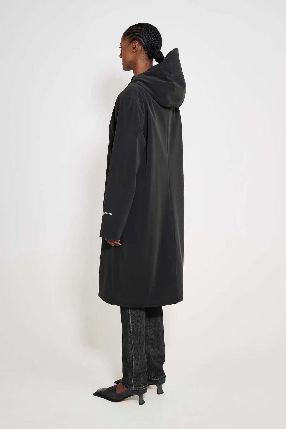 Stockholm Long Patch Black Raincoat shown from the back, featuring an oversized fit and adjustable hood.