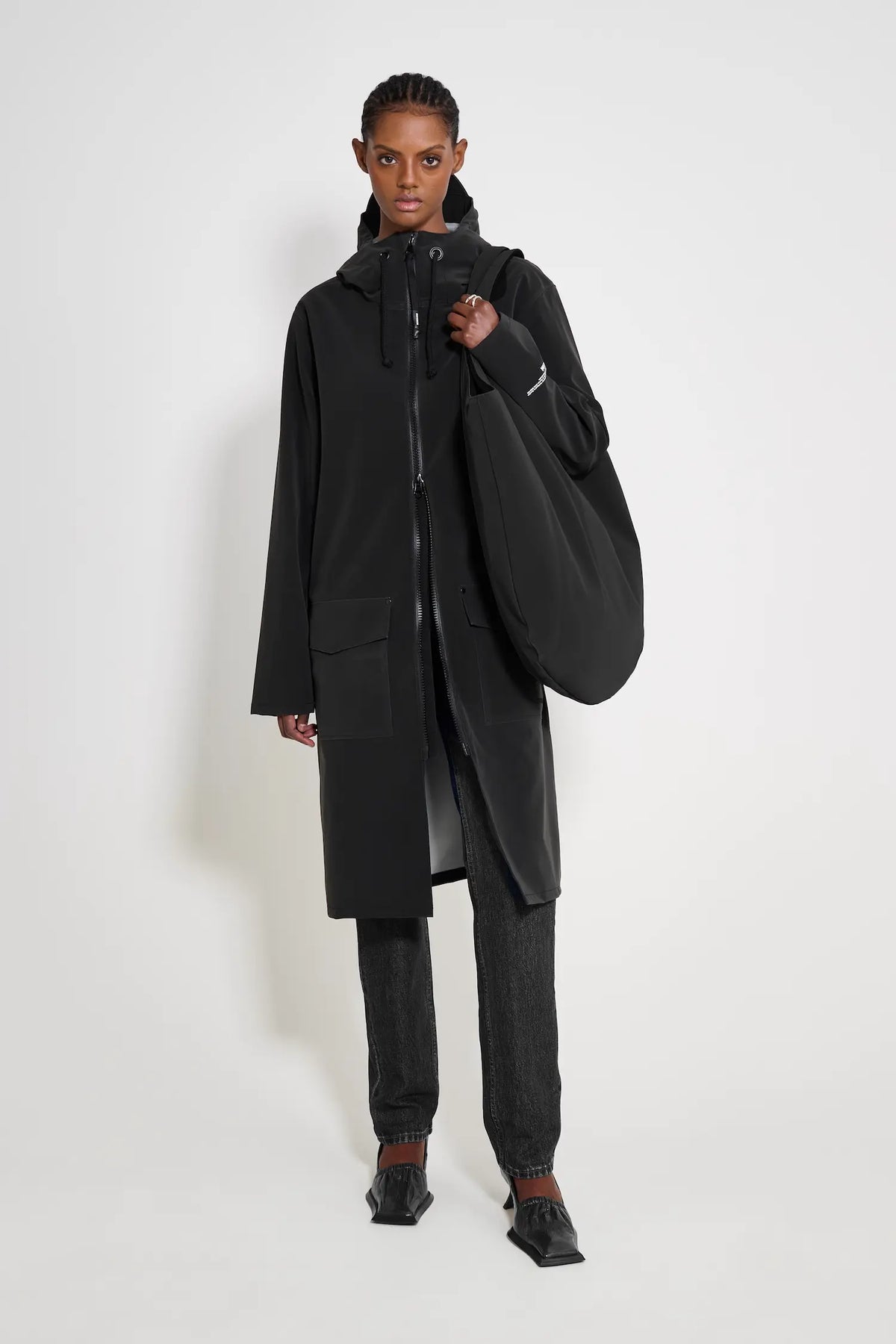 Model wearing the Stockholm Long Patch Black Raincoat with adjustable hood and flaps, showcasing its waterproof features.
