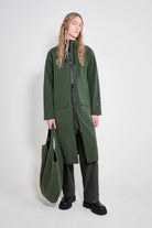 Stockholm Long Patch Matte Green Raincoat worn by a model with a tote bag, showcasing its stylish and waterproof design.