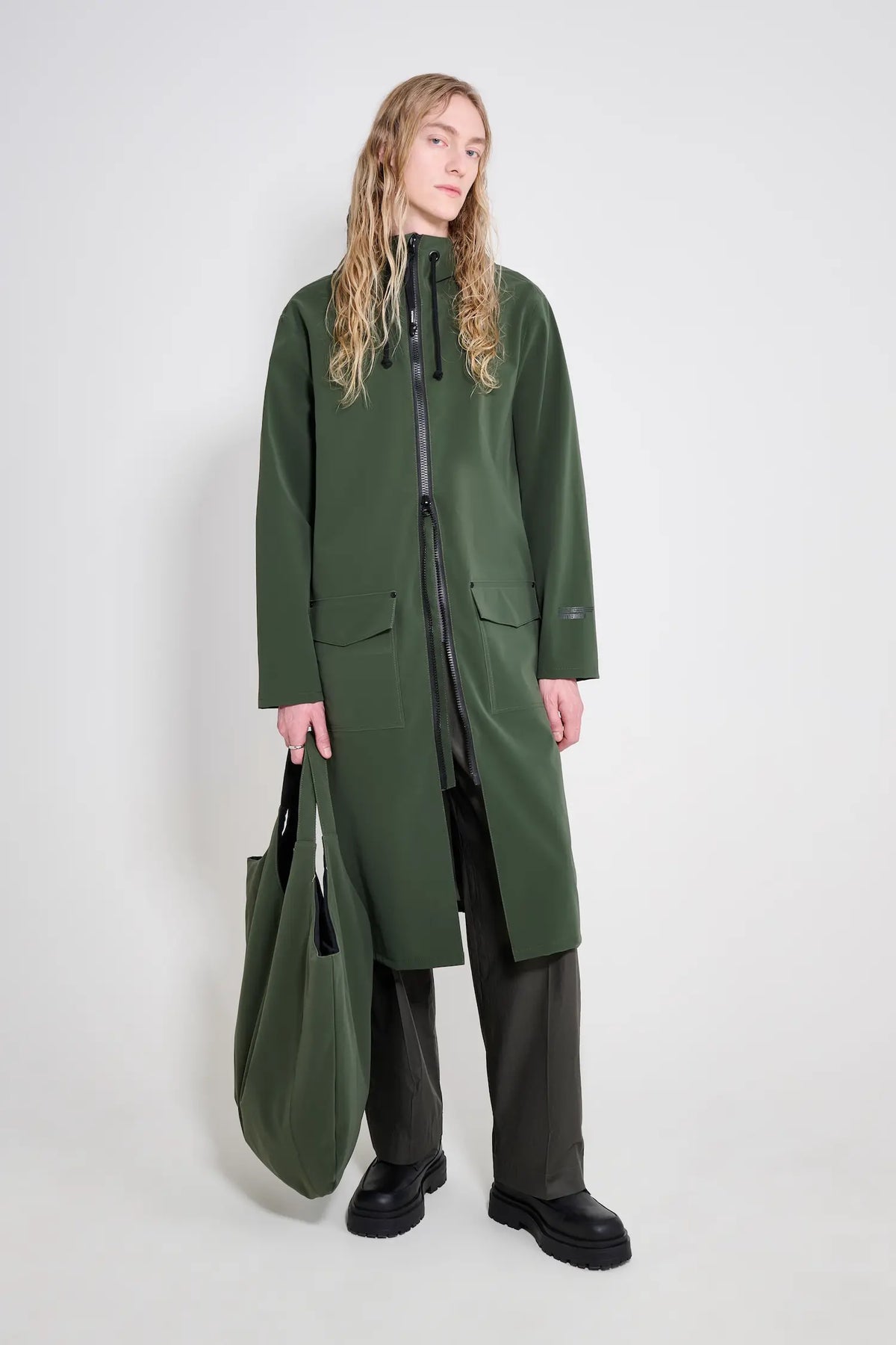 Stockholm Long Patch Matte Green Raincoat worn by a model with a tote bag, showcasing its stylish and waterproof design.