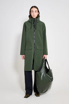 Model wearing Stockholm Long Patch Matte Green Raincoat with a black bag, showcasing a stylish and functional raincoat design.