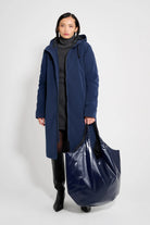 Stockholm Long Matte Navy Winter Coat worn by a model with a large blue tote bag on a neutral background.