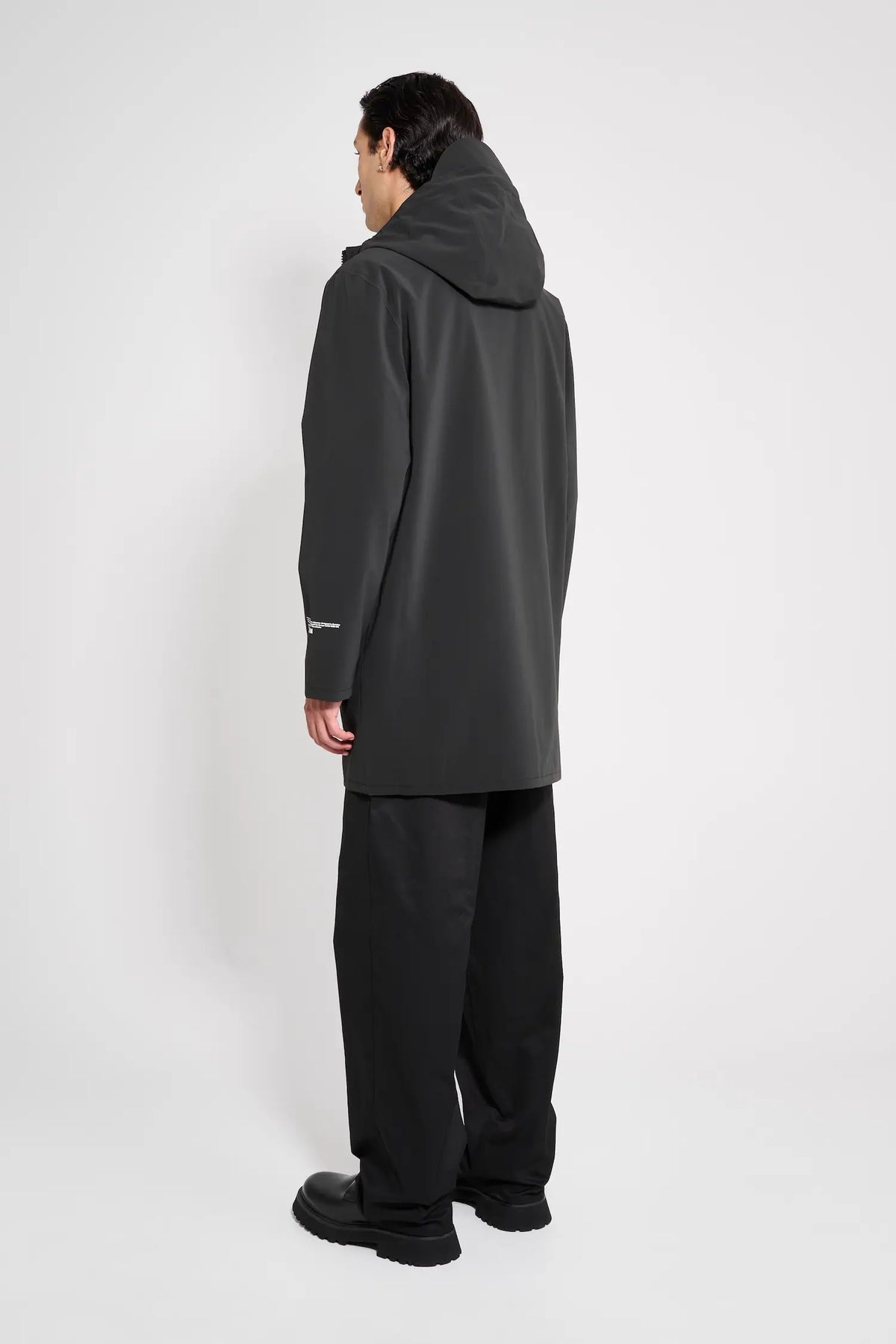 Stockholm Patch Black Raincoat displayed on a model from the back, showcasing its oversized fit and adjustable hood.