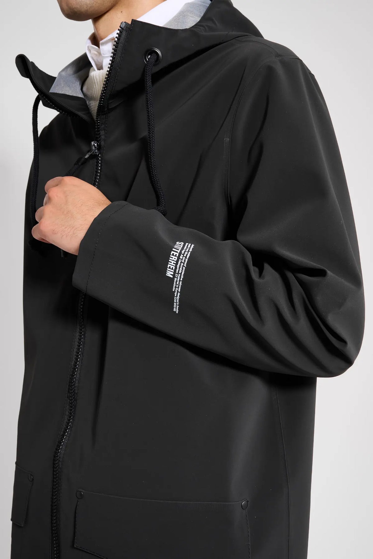 Stockholm Patch Black Raincoat on model showcasing the adjustable drawstring hood and sleek design.