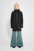 Model wearing the Stockholm Patch Black Raincoat in black, paired with stylish wide-leg pants.