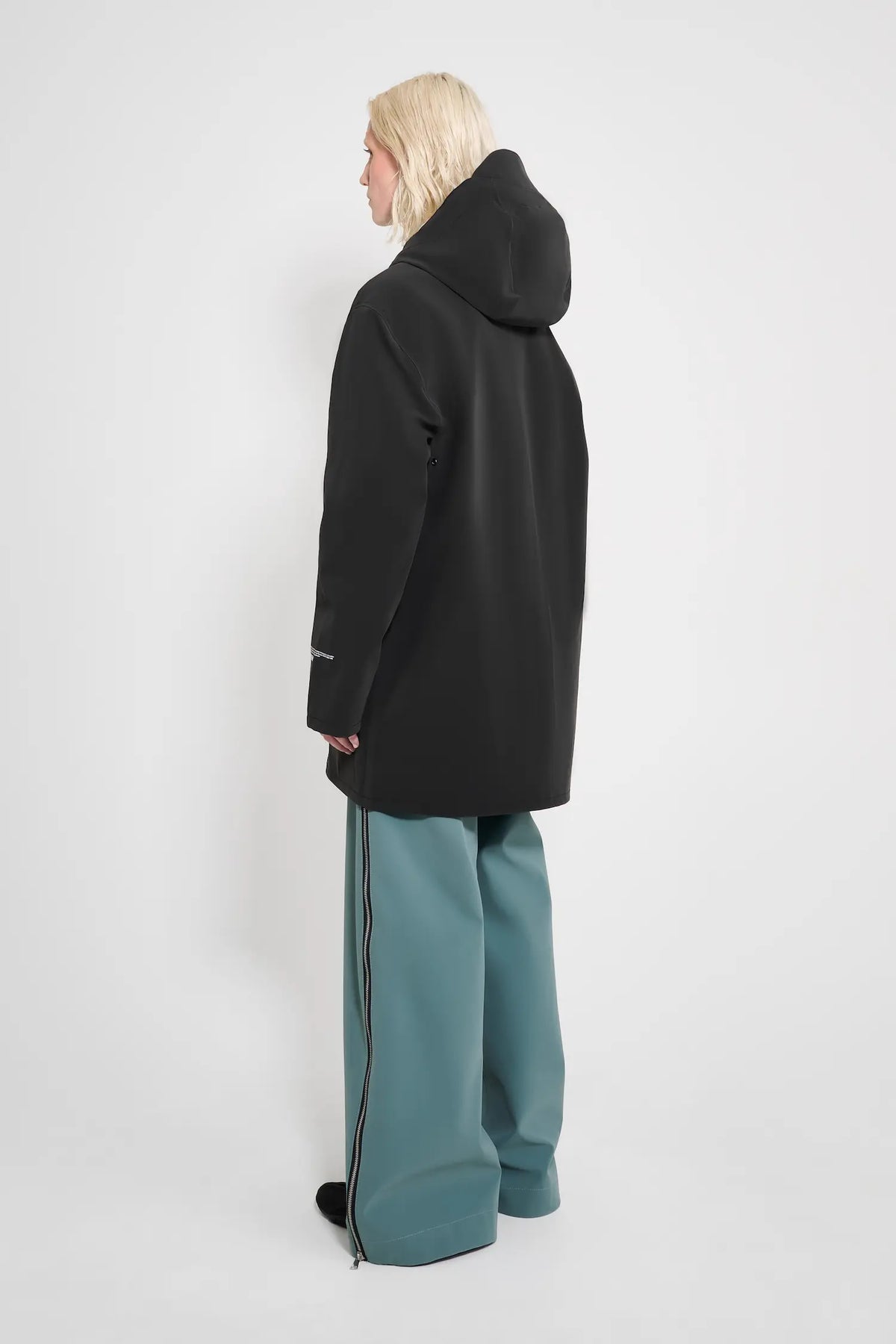 Model wearing the Stockholm Patch Black Raincoat in black, showcasing the back view with adjustable hood.