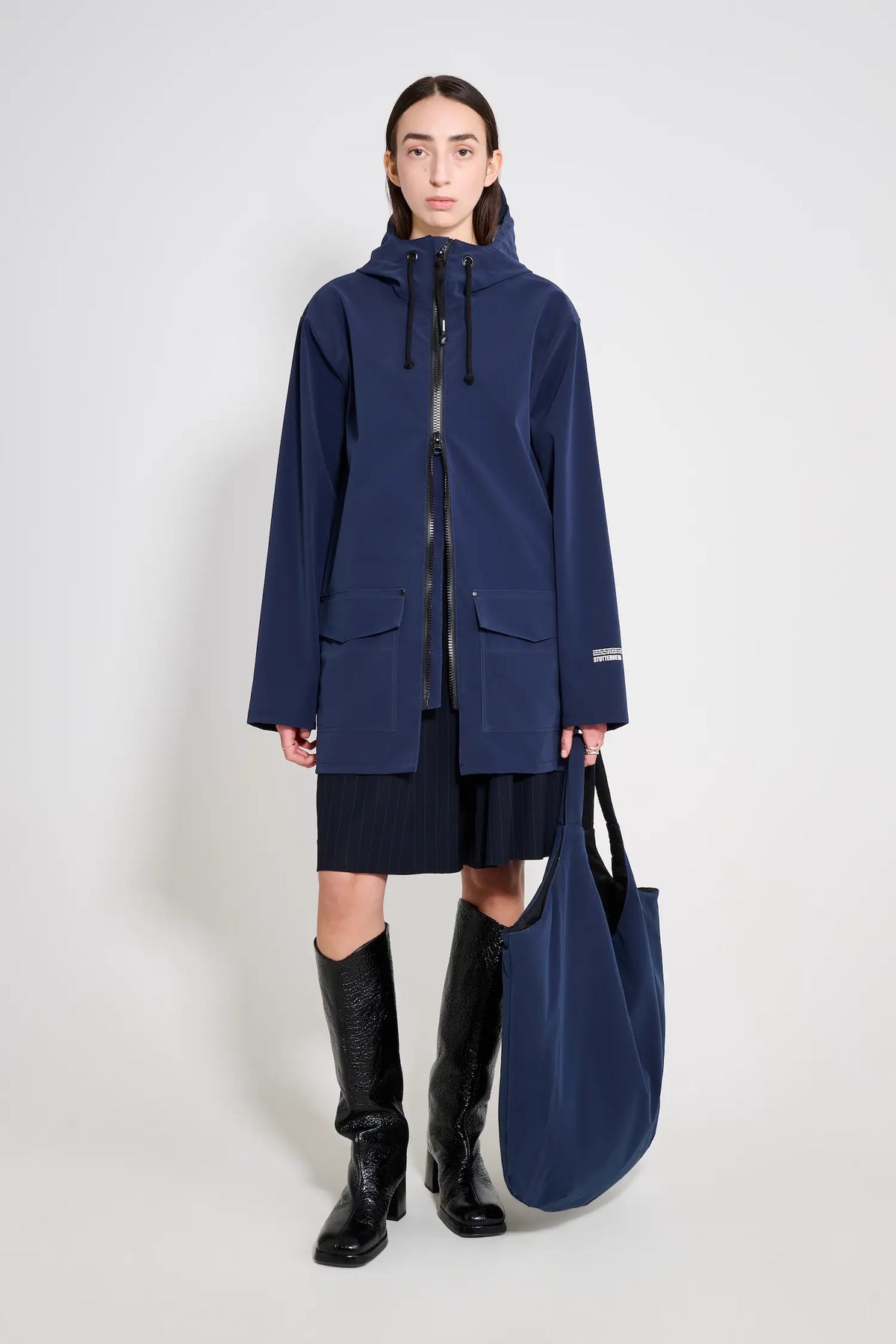 Model wearing Stockholm Patch Navy Raincoat with adjustable hood and flaps, paired with a stylish tote bag.
