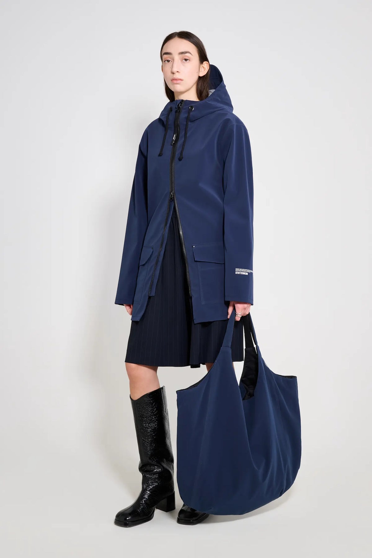 Model wearing a Stockholm Patch Navy Raincoat with a large navy bag, showcasing a stylish unisex design.
