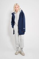 Model wearing the Stockholm Patch Navy Raincoat, a completely waterproof oversized rain jacket, styled with gray pants and boots.