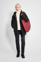 Model wearing Stockholm Matte Black Winter Coat with a red bag, styled for winter fashion.