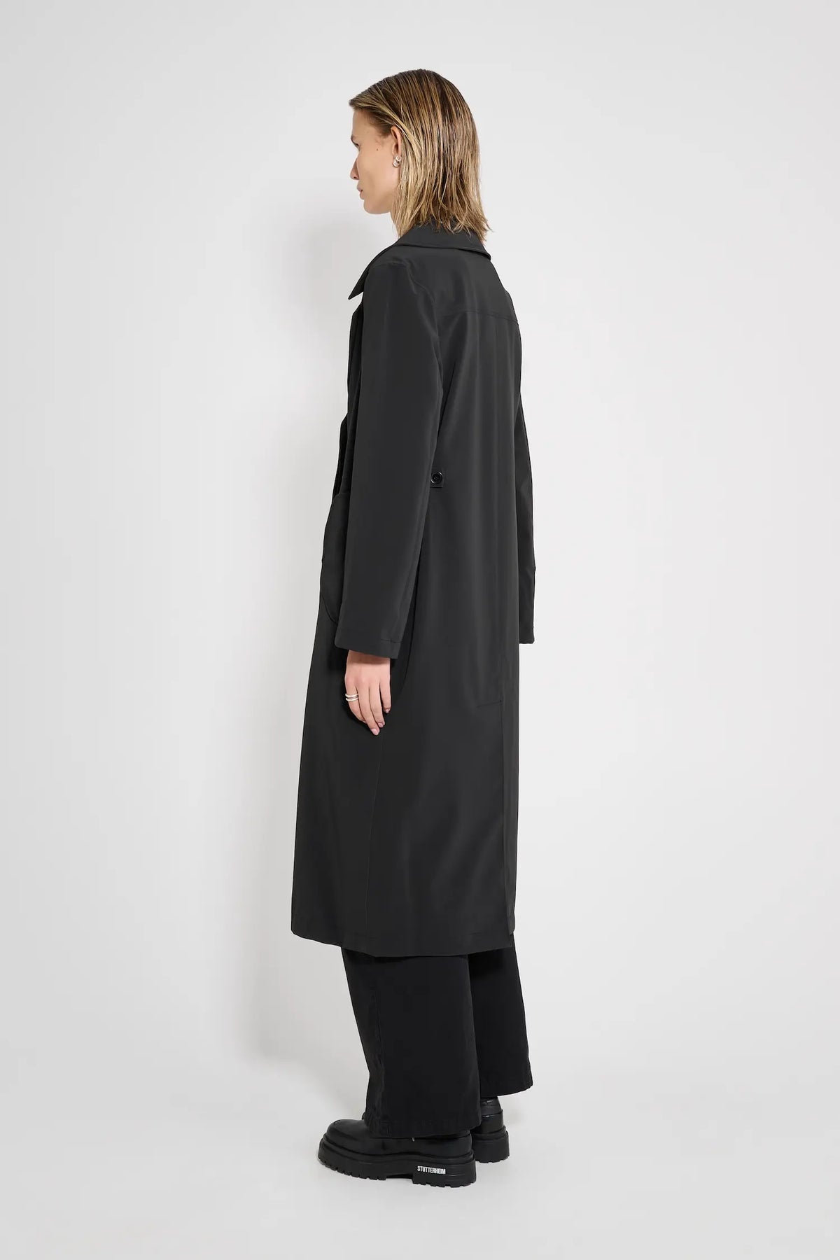Model wearing Wayfair Black Trench Coat, showcasing its sleek design and oversized fit from the side.